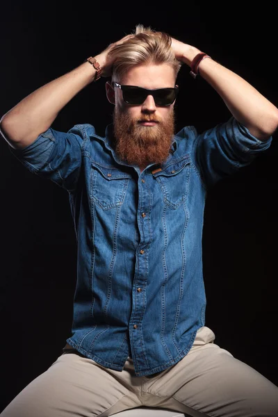 Hombre guapo sentado y fijándose el pelo con ambas manos — Foto de Stock