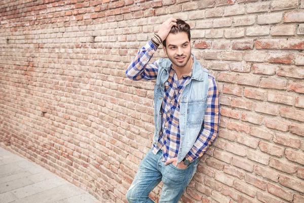 Uomo appoggiato su un muro di mattoni mentre fissa i capelli — Foto Stock