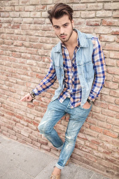 Uomo in jeans appoggiato a un muro di mattoni — Foto Stock