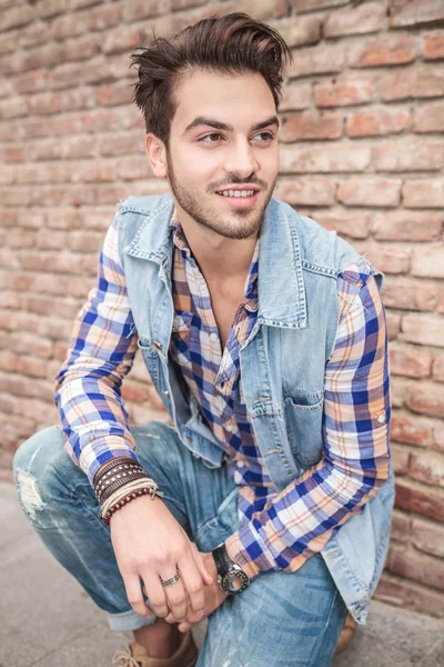 Hombre guapo sentado cerca de una pared de ladrillo — Foto de Stock