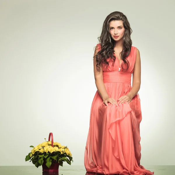 Woman in red dress is sitting near yellow flowers basket — Stock Photo, Image