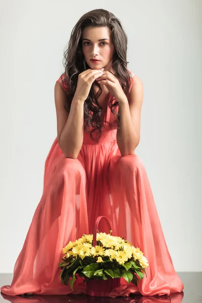 Sexy seated woman in red dress is thinking near flowers — Stock Photo, Image