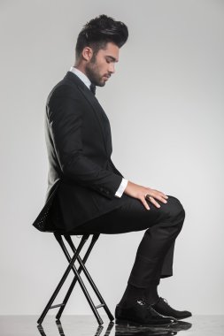 elegant young man sitting on a stool looking down clipart