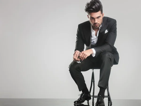 Elegant young man in tuxedo sitting on a stool — Stock Photo, Image