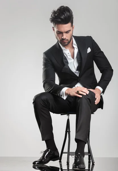 Elegant young man stitting on a stool while looking down — Stock Photo, Image