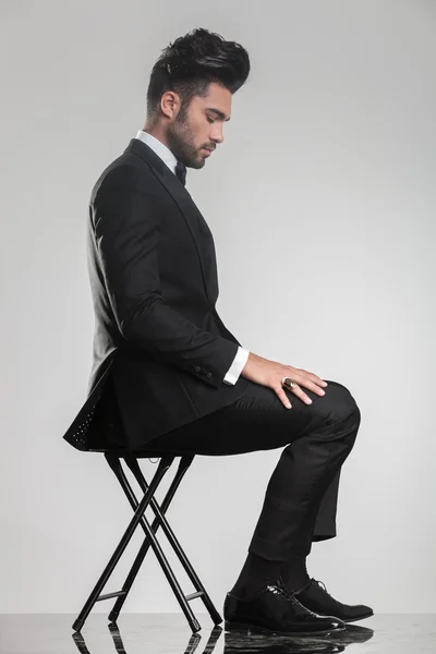 Elegant young man sitting on a stool looking down — Stock Photo, Image