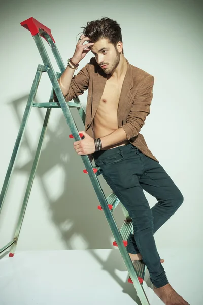 Homem de moda inclinando-se para uma escada enquanto fixa seu cabelo — Fotografia de Stock