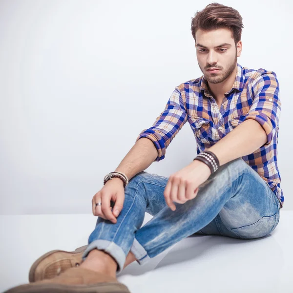 Junger Mann schaut auf dem Boden sitzend nach unten — Stockfoto