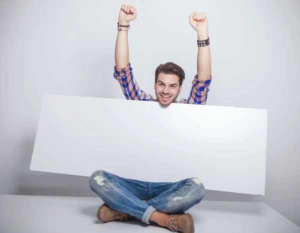 Uomo di moda seduto mentre tiene un cartellone vuoto . — Foto Stock