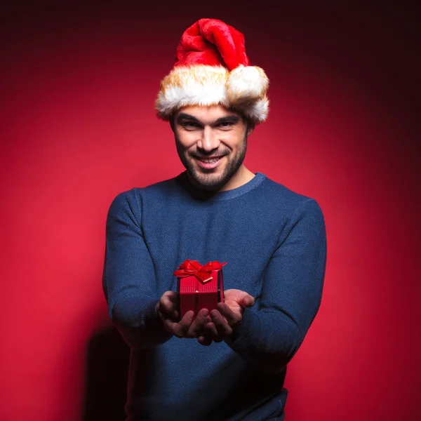 Attractive young santa giving you a small red gift — Stock Photo, Image