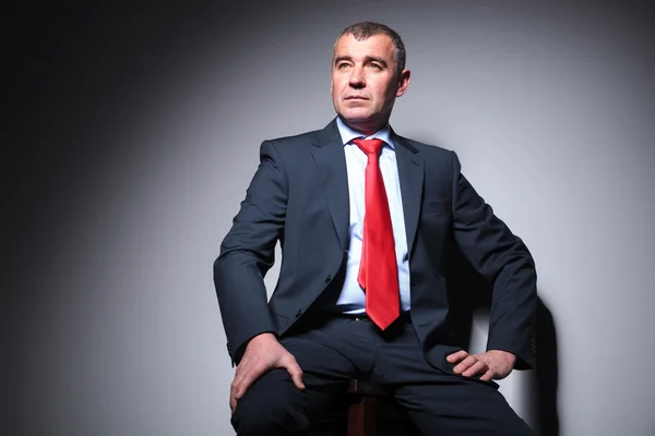 Hombre de negocios sentado en un taburete, sobre fondo gris . — Foto de Stock