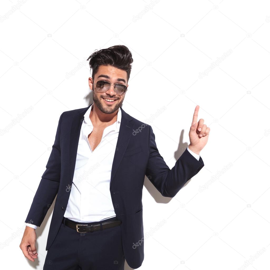 business man wearing sunglasses smiling and pointing up