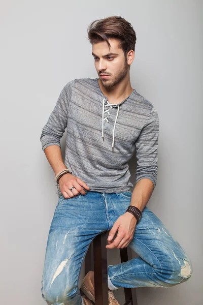 Fashion man looking down while sitting on a stool — Stock Photo, Image