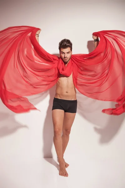 Young naked man creating wings with a red textile — Stock Photo, Image