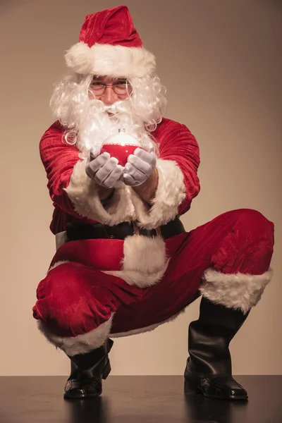 Santa sitting and presenting christmas ball. — Stock Photo, Image