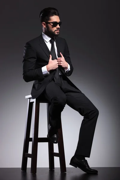 Business man sitting on a stool while fixing his jacket — Stock Photo, Image