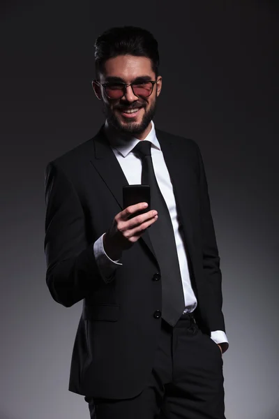 Geschäftsmann lächelt, während er ein Telefon in der Hand hält — Stockfoto
