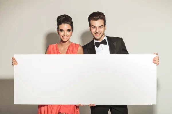 Élégant couple souriant tout en tenant un tableau blanc — Photo