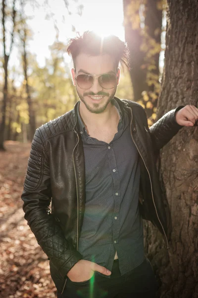 Smiling fashion man leaning on a tree. — Stock Photo, Image