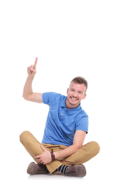 Seated young casual man points upwards — Stock Photo, Image