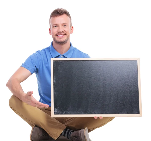 Genç oturan adam boş yazı tahtası sunar — Stok fotoğraf