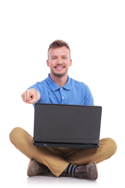 young seated man with laptop points at you