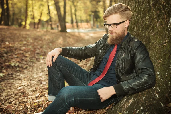 Atractivo joven hombre de la moda sentado en el parque — Foto de Stock