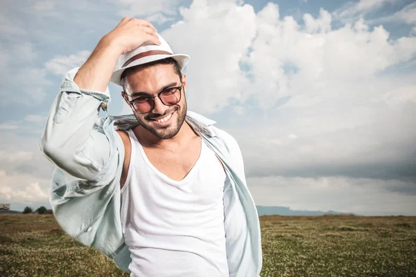 Smiling young fashion man holding his hat — Stock Photo, Image