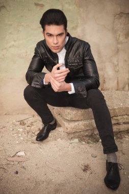 bir duvara yakın oturan yakışıklı genç moda adam 