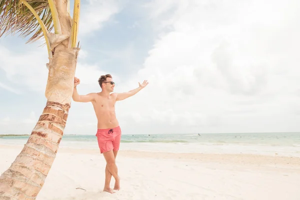 Smiling lifeguard leaning on a palm tree