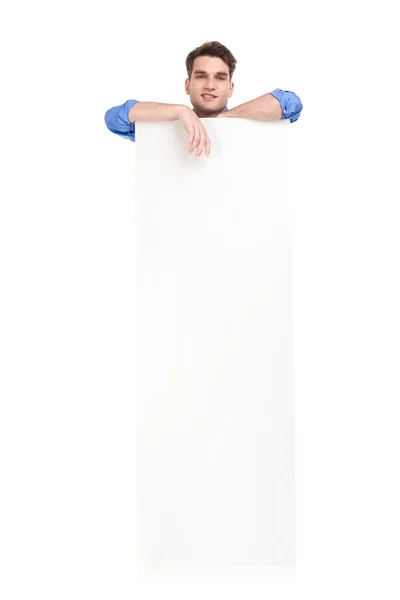 Bonito homem encostado em um branco vazio banner — Fotografia de Stock