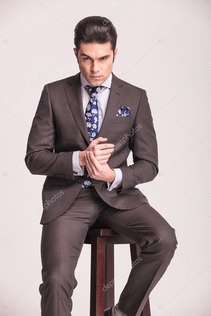business man sitting on a stool holding his hands together.