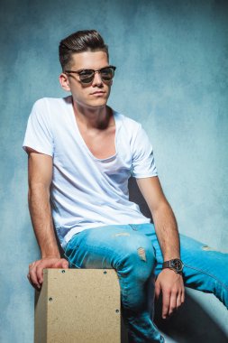 Tahta bir kutu üzerinde oturan düşünceli genç adam