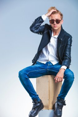 man posing wearing sunglasses and fixing his hair while sitting
