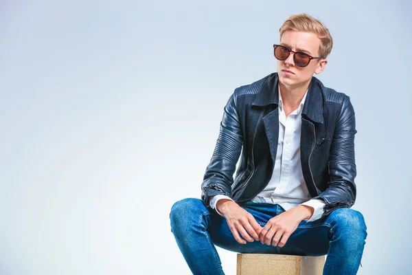 Skinny man wearing sun glasses and leather jacket while sitting — Stock fotografie