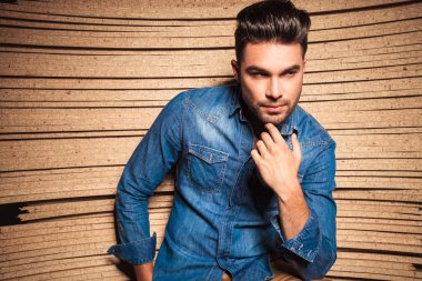 man touching his chin while leaning against a wooden wall