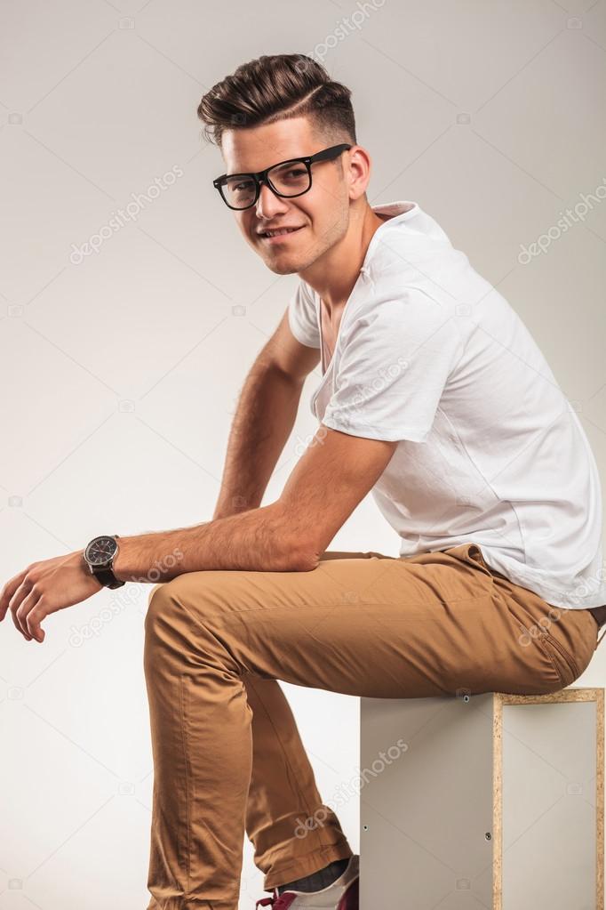 young man sitting on a box while wearing glasses