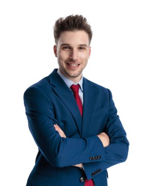 Lacivert takım elbiseli mutlu bir iş adamı kollarını kavuşturup beyaz arka planda gülümsüyor.