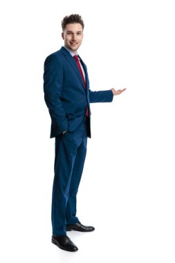 Deniz mavisi takım elbiseli mutlu genç adamın yandan görünüşü beyaz arka planda el ele dururken gülümsüyor.