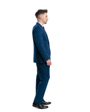 Lacivert takım elbiseli zarif bir gencin beyaz arka plan önünde kuyrukta dikilip ileriye bakması.