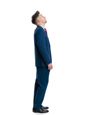 Mavili lacivert takım elbiseli zarif genç işadamının yan görüntüsü beyaz arka planın önünde duruyor.