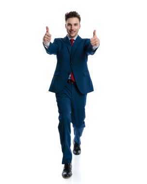 Lacivert takım elbiseli mutlu bir iş adamı beyaz arkaplan önünde yürüyor ve baş parmak hareketi yapıyor.