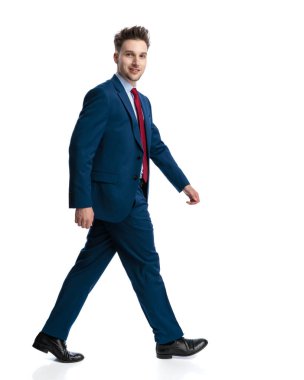Lacivert takım elbiseli, beyaz arka planda yürüyen ve gülümseyen mutlu zarif iş adamının yan görüntüsü.