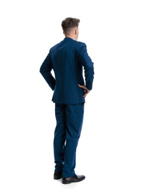 Lacivert takım elbiseli zarif genç işadamının dikiz aynasından beyaz arka planda elleri kalçalarının üzerinde duruyor.