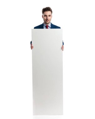 Lacivert takımlı gururlu genç işadamı boş tahtayı gösteriyor ve sunuyor ve beyaz arkaplan önünde gülümsüyor.