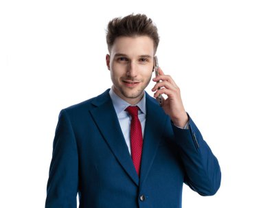 Lacivert takımlı çekici bir iş adamı telefonda konuşuyor ve beyaz arka planda gülümsüyor.