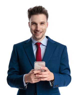 Lacivert takımlı, mutlu, zarif bir adam. Beyaz arka plan önünde gülümseyip mesajlaşıyor.