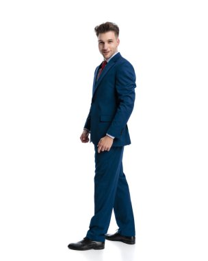 Lacivert takımlı mutlu, zarif bir adam yürüyor, ileriye bakıyor ve beyaz arka planda gülümsüyor.