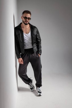 Siyah deri ceketli seksi genç adam duvara yaslanıyor ve gri arka planda el ele tutuşuyor.