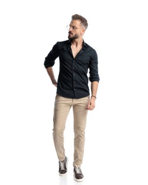 Gözlüklü, siyah gömlekli, beyaz arka planda yürüyen seksi bir adam.